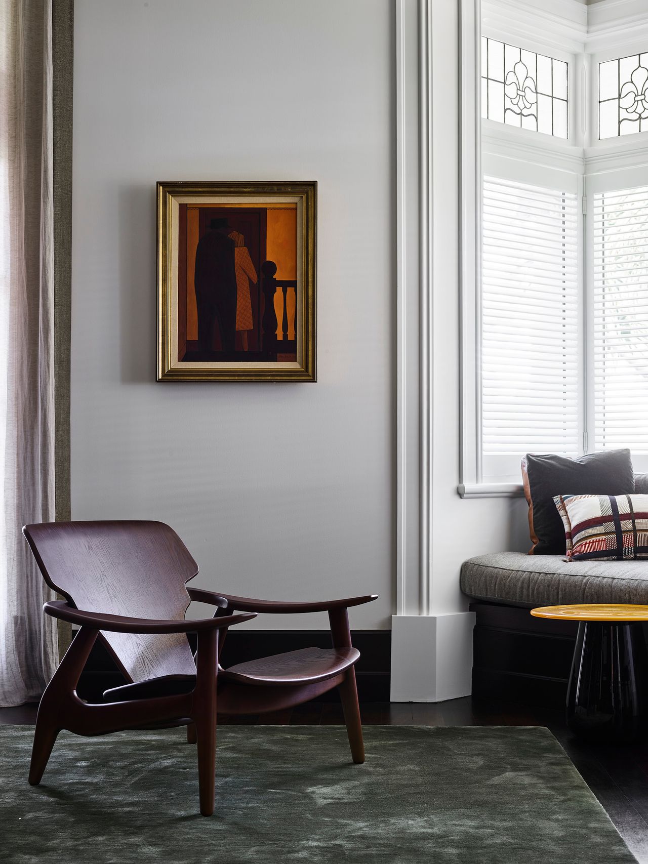 Sculptural timber armchair and curated artwork sit alongside original leadlight windows and a built-in window seat in this heritage coastal interior by Decus.