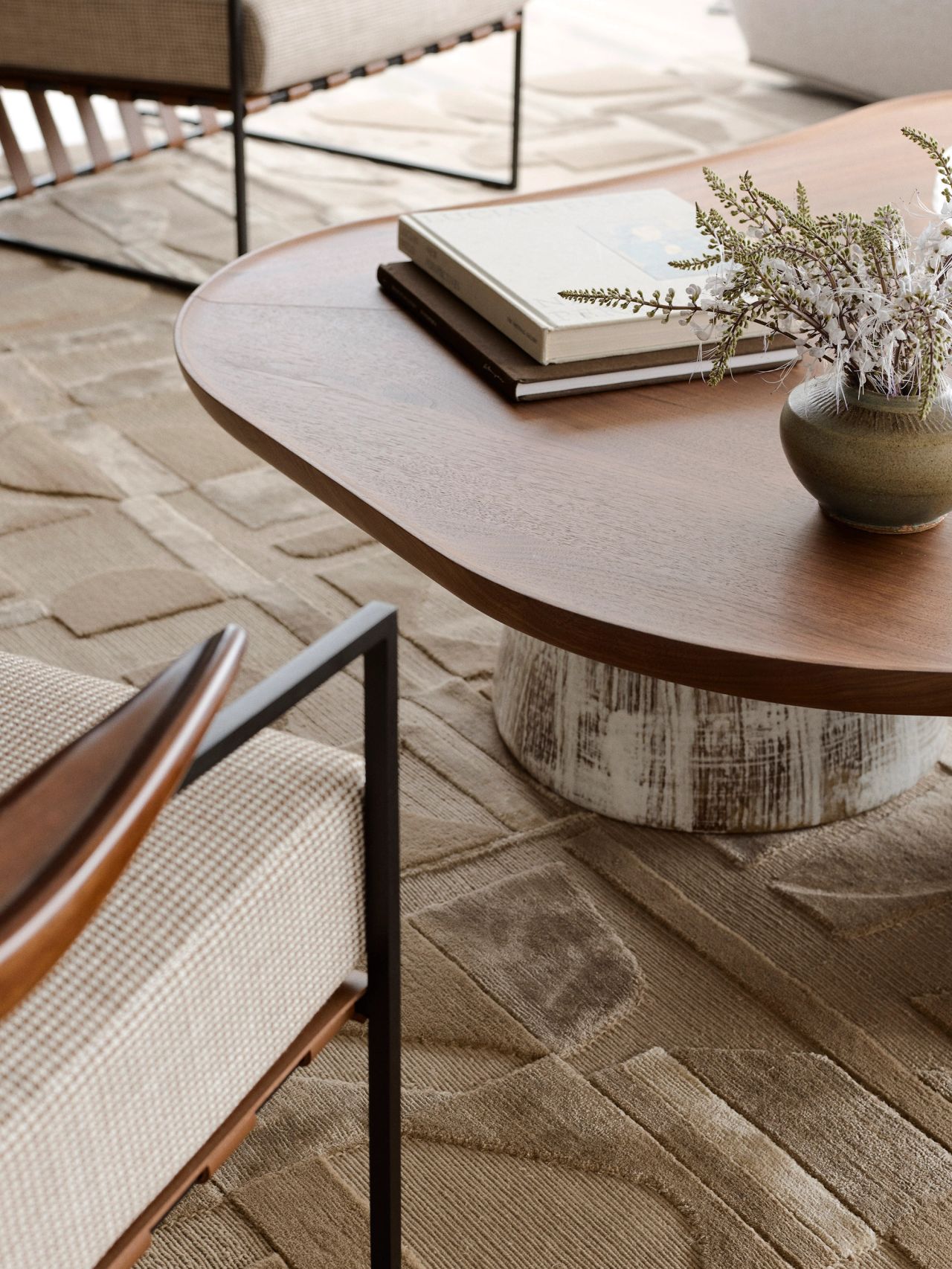Orla contemporary open-plan living room blending Brazilian influences, with a walnut coffee table on cream-glazed ceramic legs beside a Brazilian-style occasional chair with beige upholstery and timber arm detailing, both sitting on a cream geometric-patterned rug.