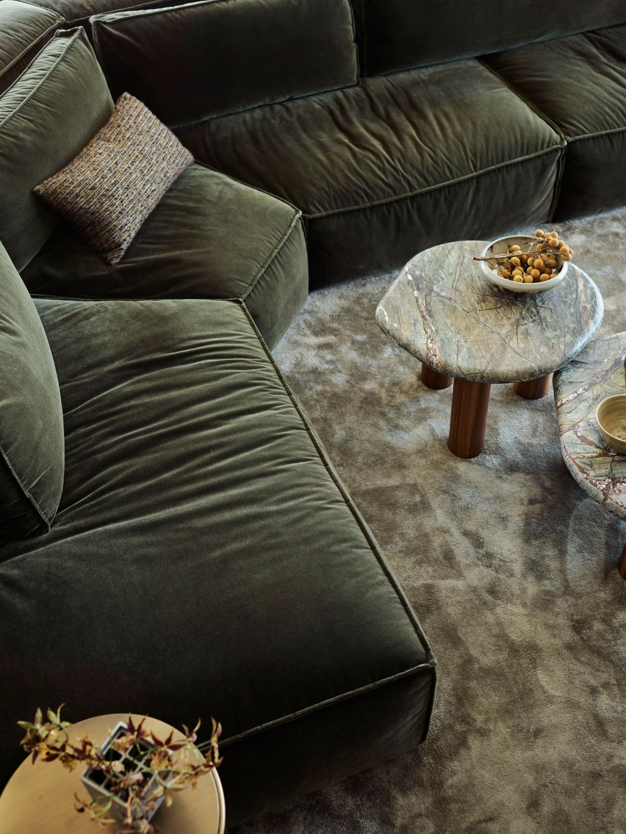 Deep olive modular sofa, sculptural natural stone tables and soft silk rug feature in this intimate Broadbeach lounge room by Decus.