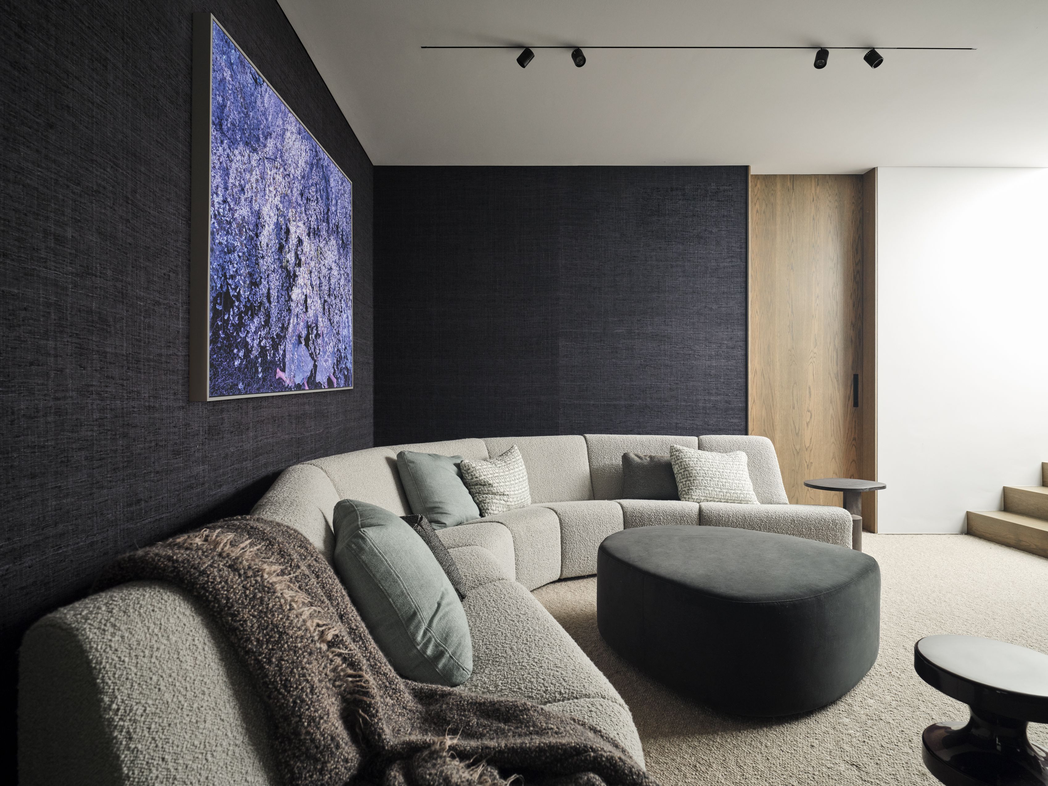 Intimate media room with curved boucle sectional sofa, dark textured walls, oversized artwork and soft olive cushions.