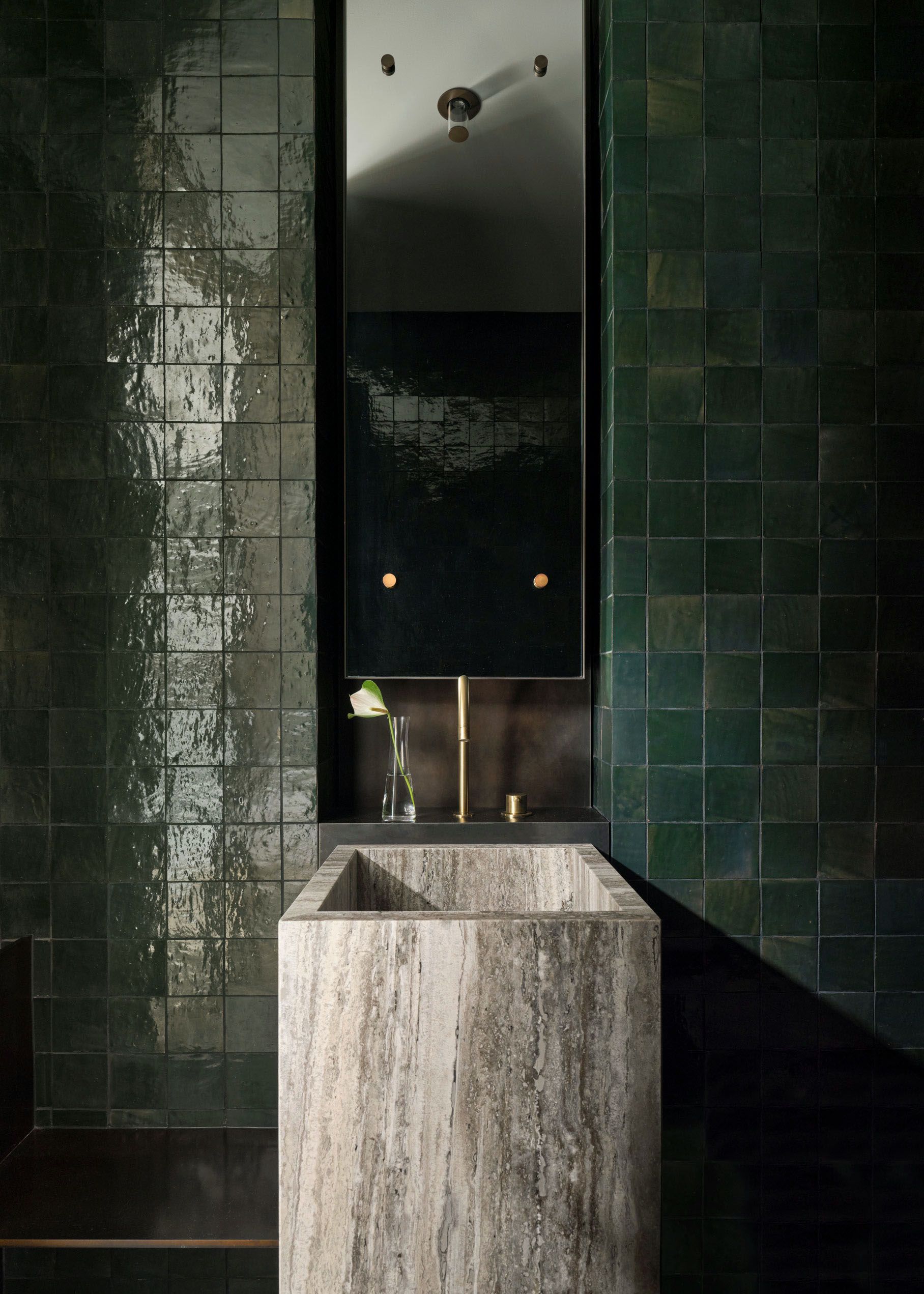 Contemporary powder room with glossy deep green tiled walls, a sculptural stone basin, brass tapware and tall mirror.