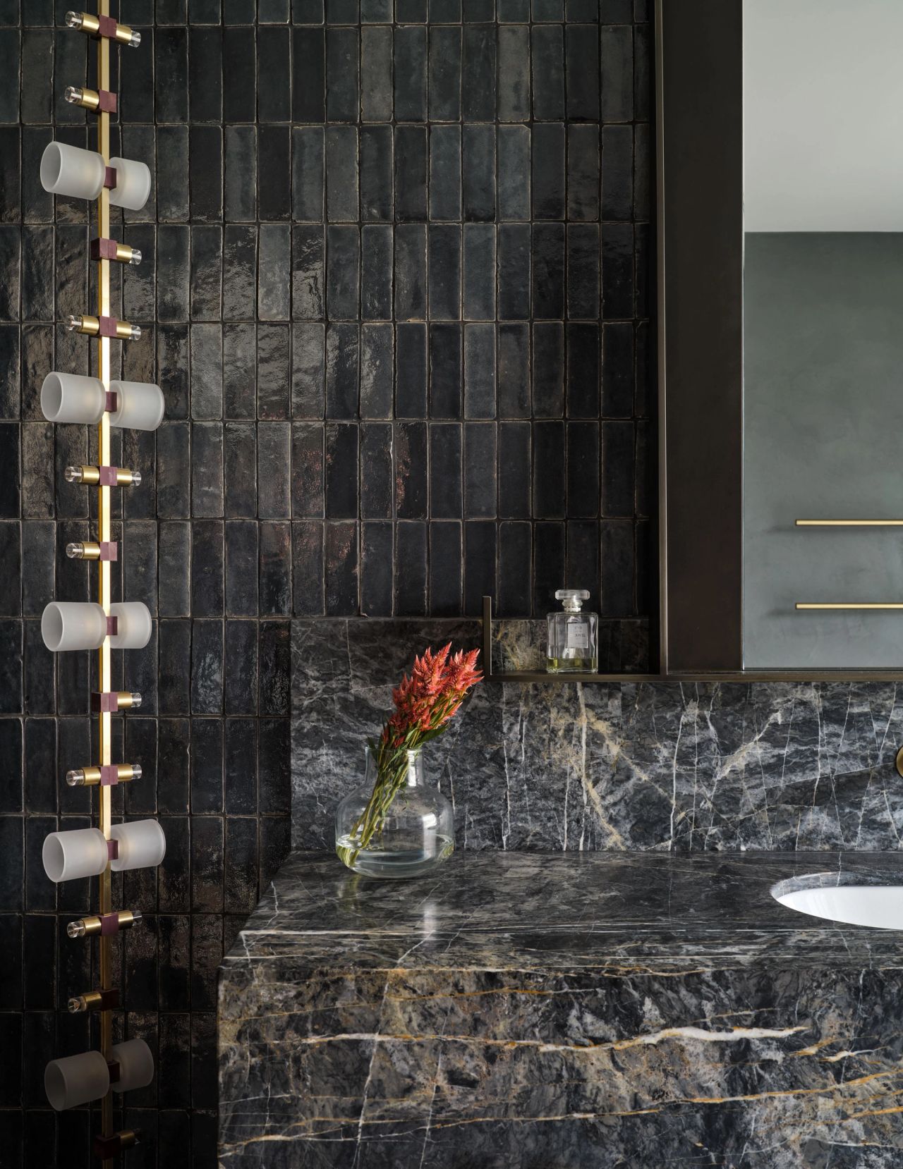 Dramatic bathroom composition pairing richly veined dark marble with glossy handmade tiles, warm brass detailing and sculptural lighting.
