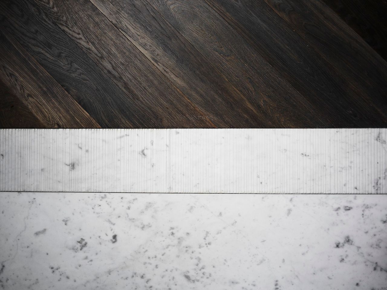 Close-up of dark timber flooring meeting a finely ribbed white marble border and pale veined stone surface.