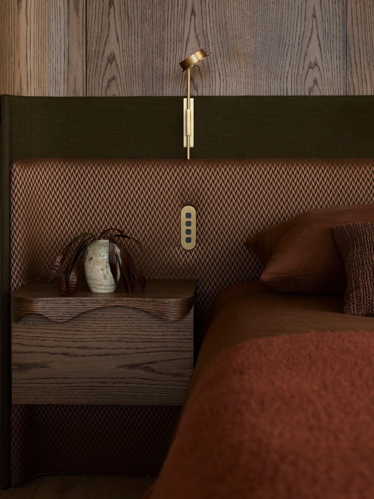 Patchwork Sculptural wooden lattice-back chair beside an arched wall niche with a black ceramic vase, opening onto a bedroom with a rust-toned bed and sheer curtains beyond