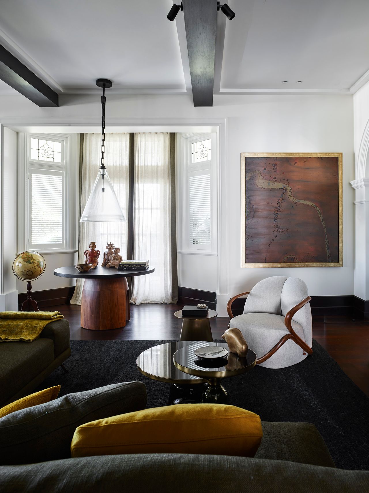 Heritage detailing meets contemporary furniture, sculptural lighting and curated art in a richly layered living room by Decus, grounded in olive, ochre and dark timber tones.