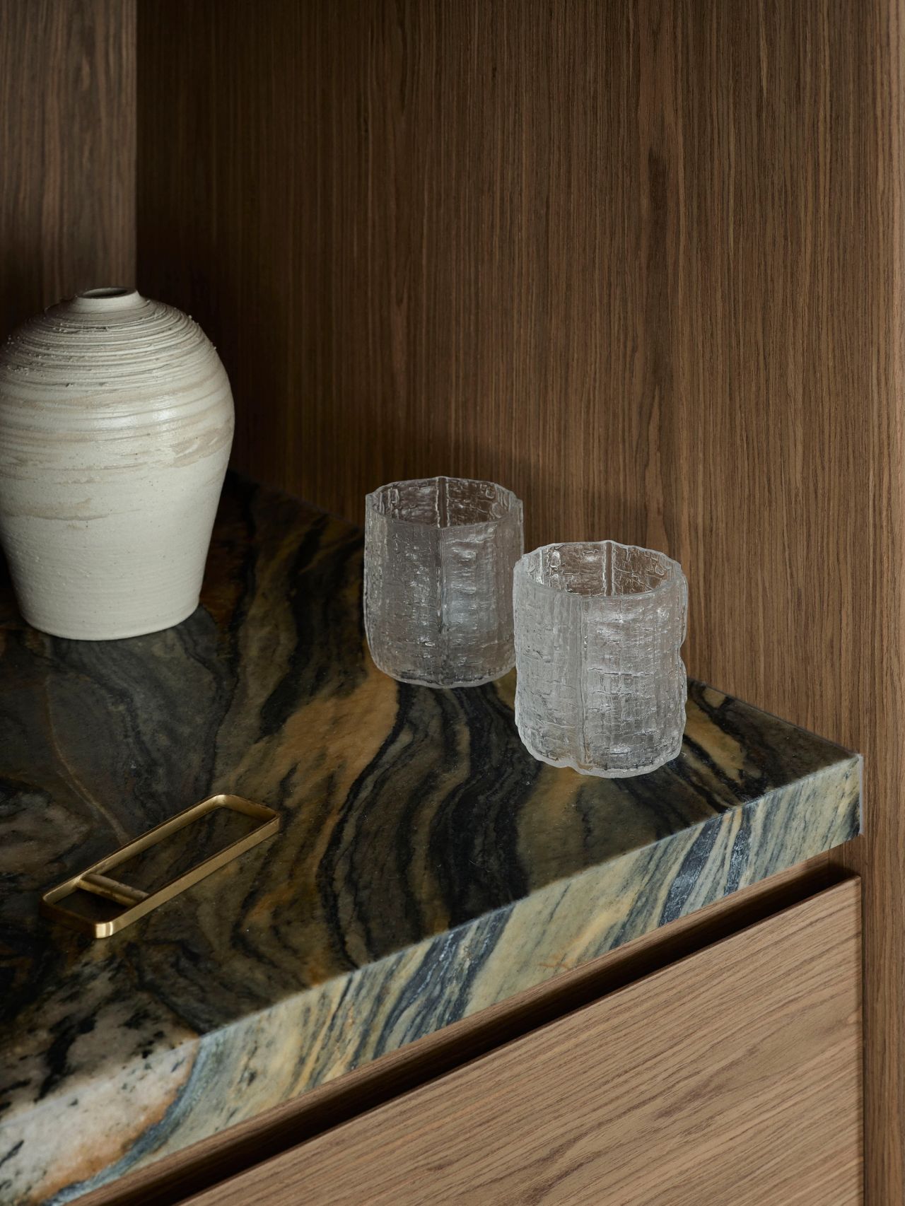 Detail of richly veined natural stone, warm timber joinery and curated ceramic and glass objects.