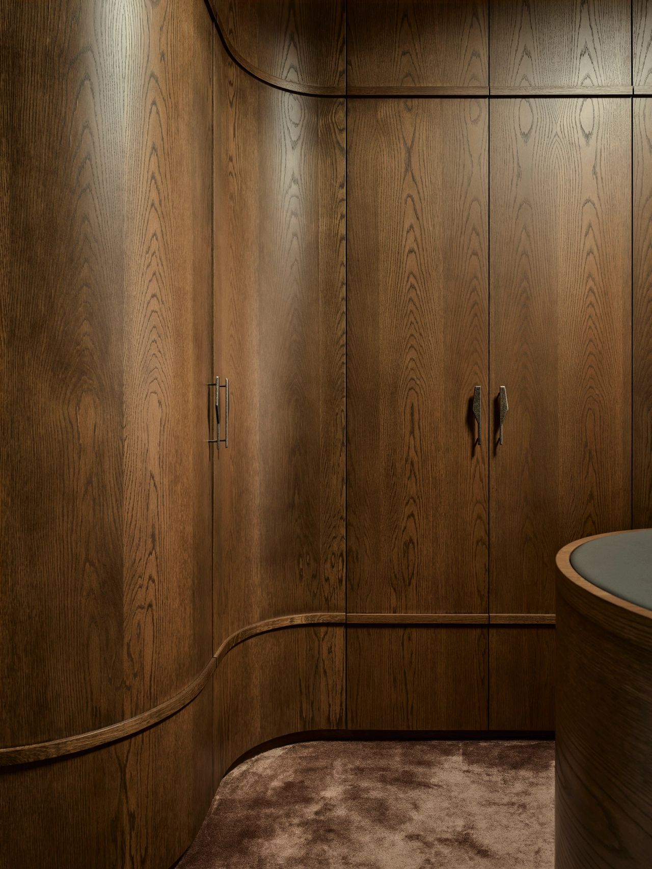 Sunset Close-up of dark oak cabinetry doors with sculptural, geometric metal handles, bronze-toned, above a curved wood detail below
