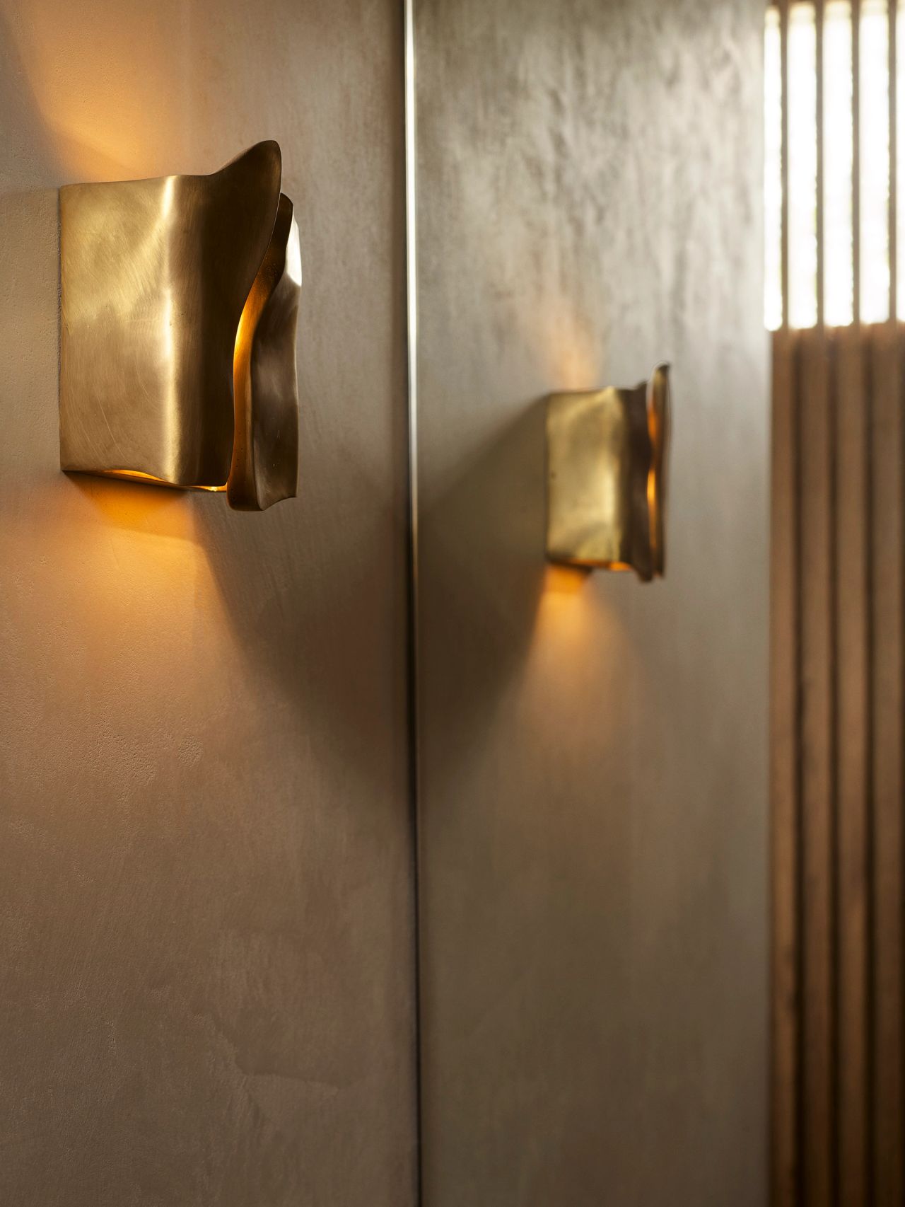 Orla powder room detail of a grey-green micro-cement rendered wall, with a brass wall light reflected in the mirror