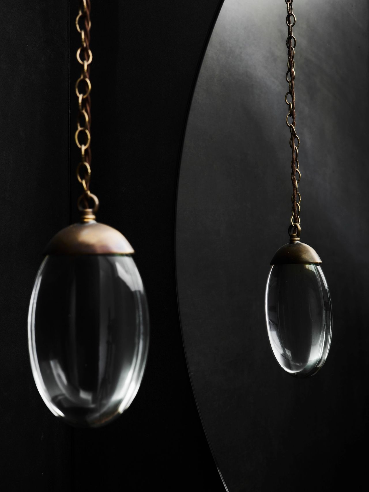 Killcare Detail of a glass and brass egg-shaped pendant light on a chain, reflected in a curved dark mirror
