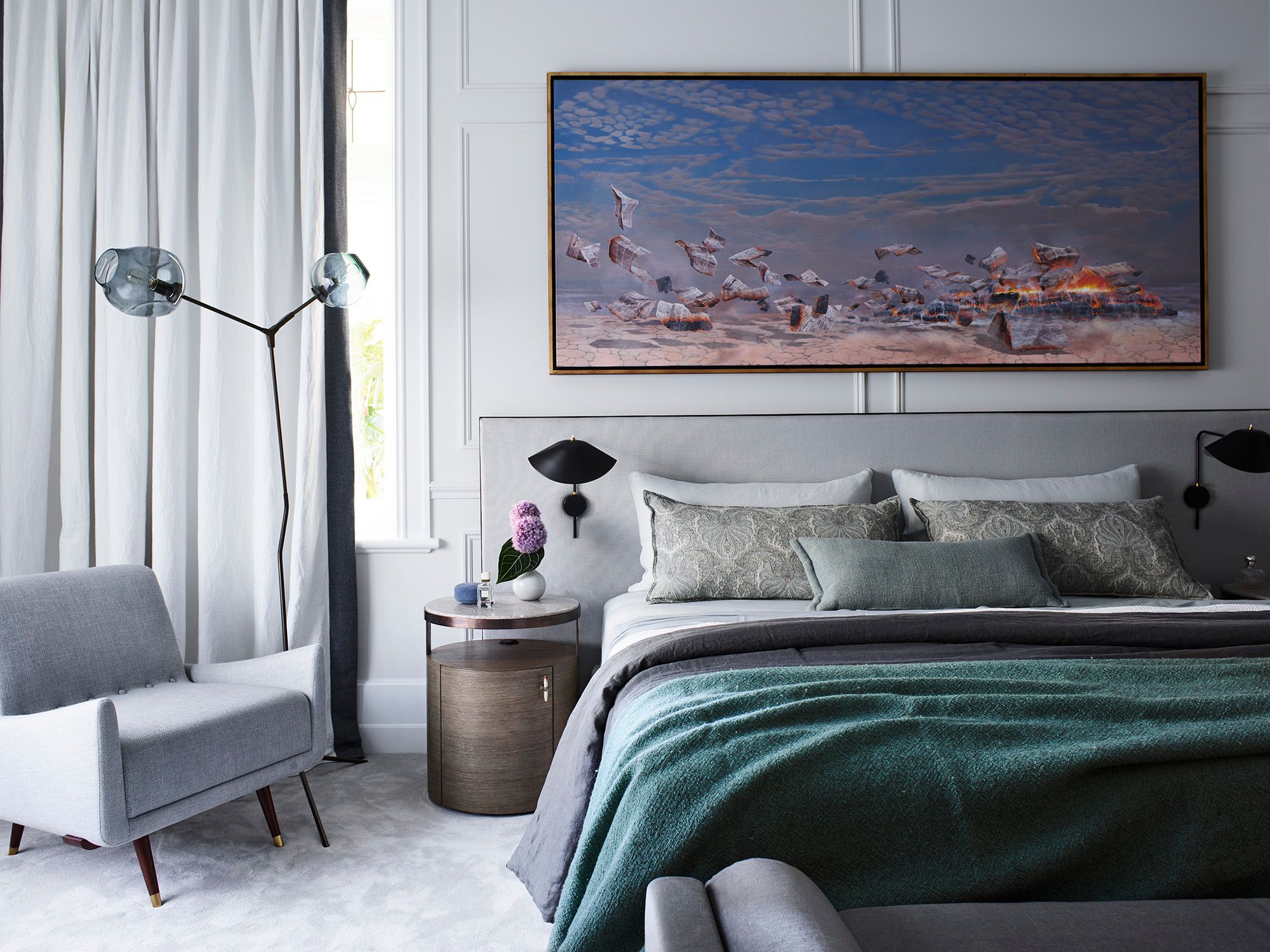 Elegant contemporary bedroom with a grey upholstered bed, deep green throw, sculptural black wall lights and large statement artwork.