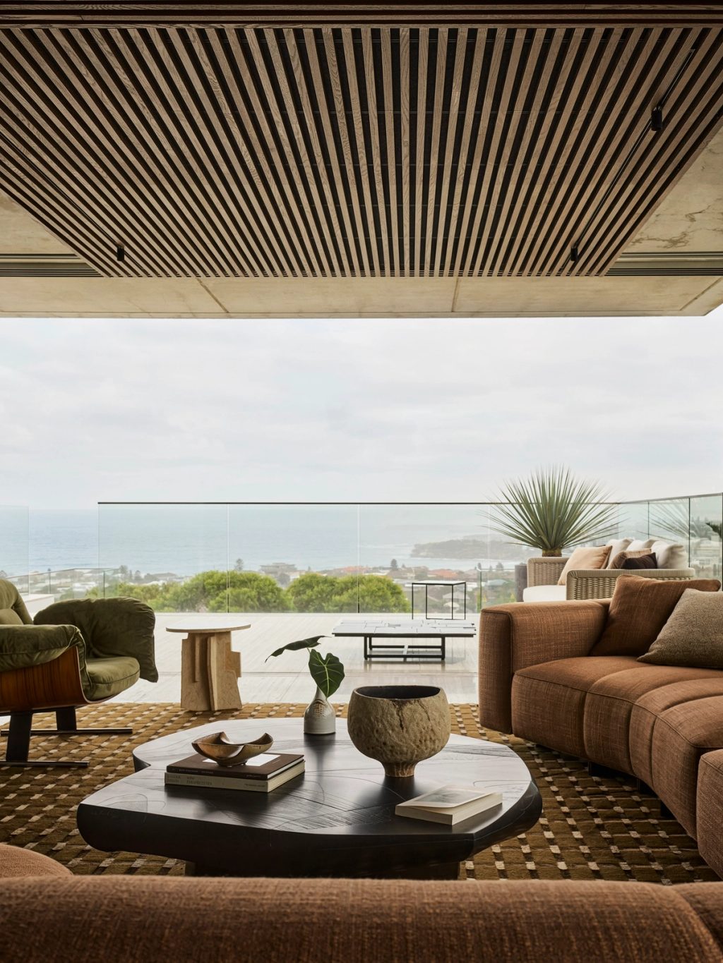 Orla_Living room with sculptural furniture, timber batten ceiling and layered natural materials overlooking sydney coastal views.