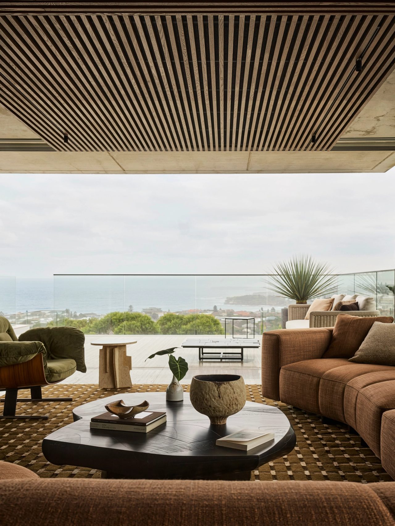 Orla Contemporary living room design blending Brazilian influences with a warm brown, black, and camel palette; Bondi Beach visible over the balcony