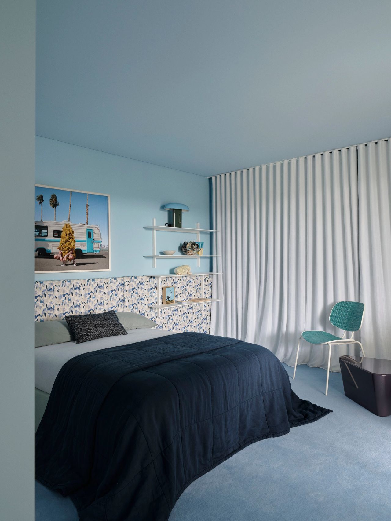 Sunset House_Contemporary blue bedroom with tonal walls and carpet, patterned bedhead, navy bedding, sculptural shelving, playful contemporary art and turquoise accent chair.