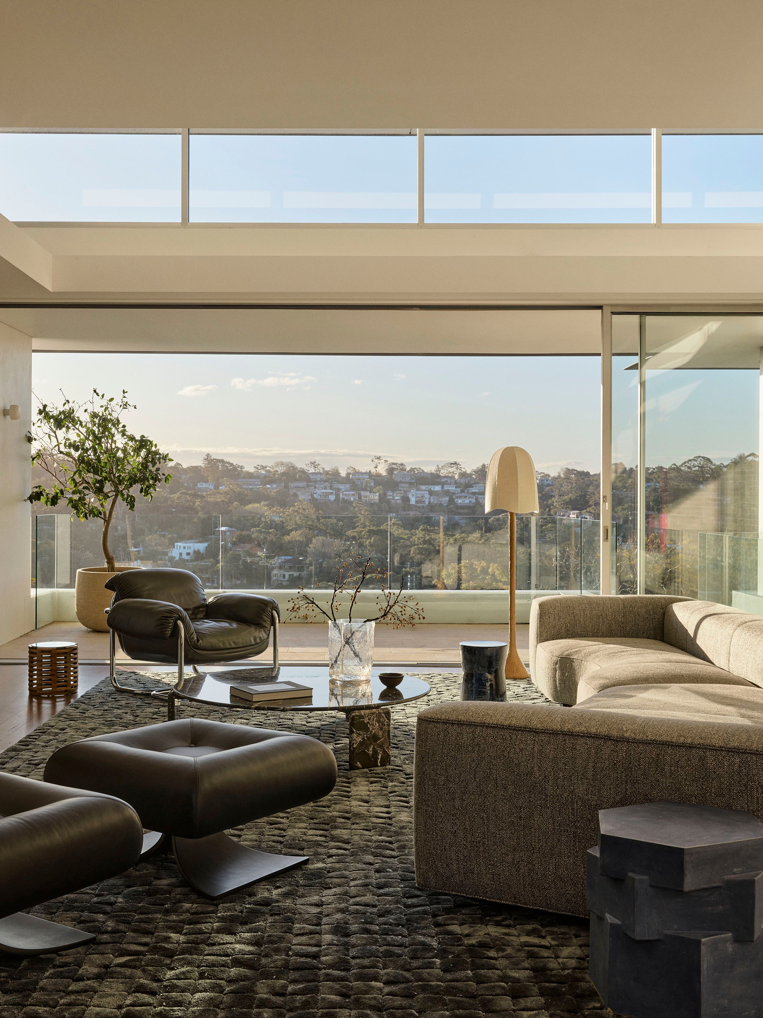 Contemporary living room by Decus Interiors in Northbridge, Sydney featuring sculptural furniture, rich natural textures and floor to ceiling glazing overlooking the surrounding landscape.