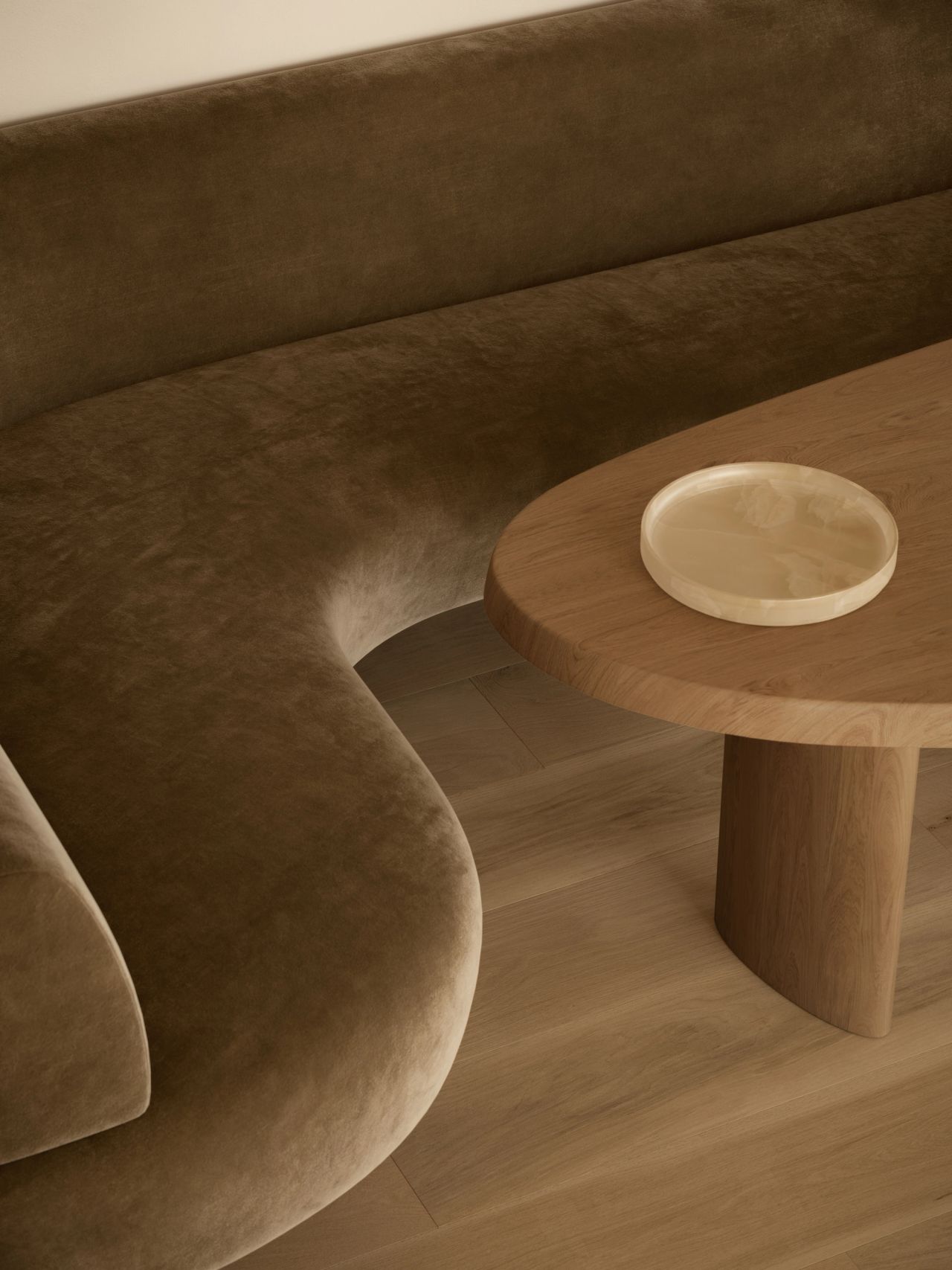 Lady M Close-up detail of a curved olive velvet banquette meeting a round timber pedestal table, with an alabaster catchall tray on top, showcasing the sculptural curves and material textures of the joinery