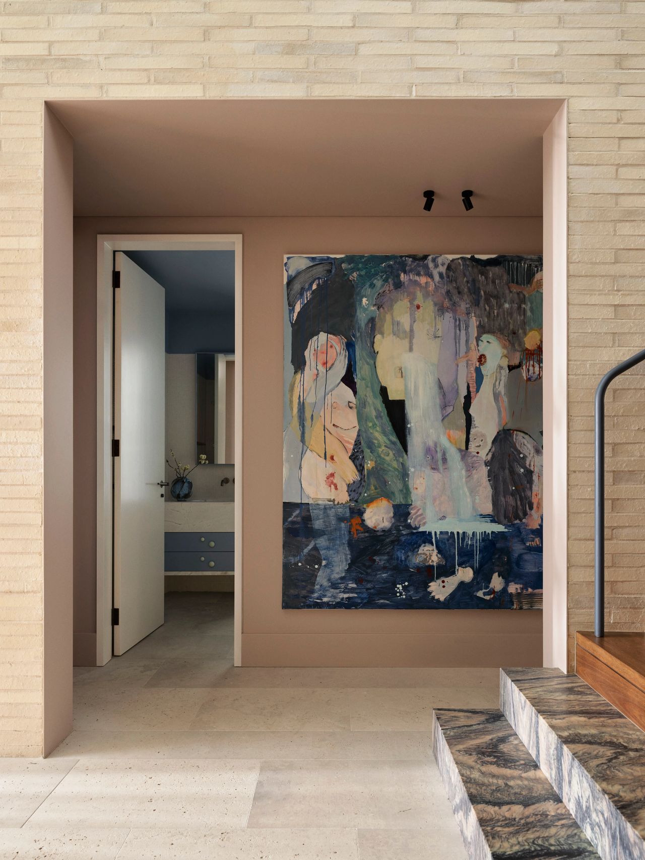 Sunset Large figurative artwork with muted blues and pastels in a dusty pink-framed nook, beside an open doorway revealing a blue bathroom vanity, with a veined marble staircase edge in the foreground