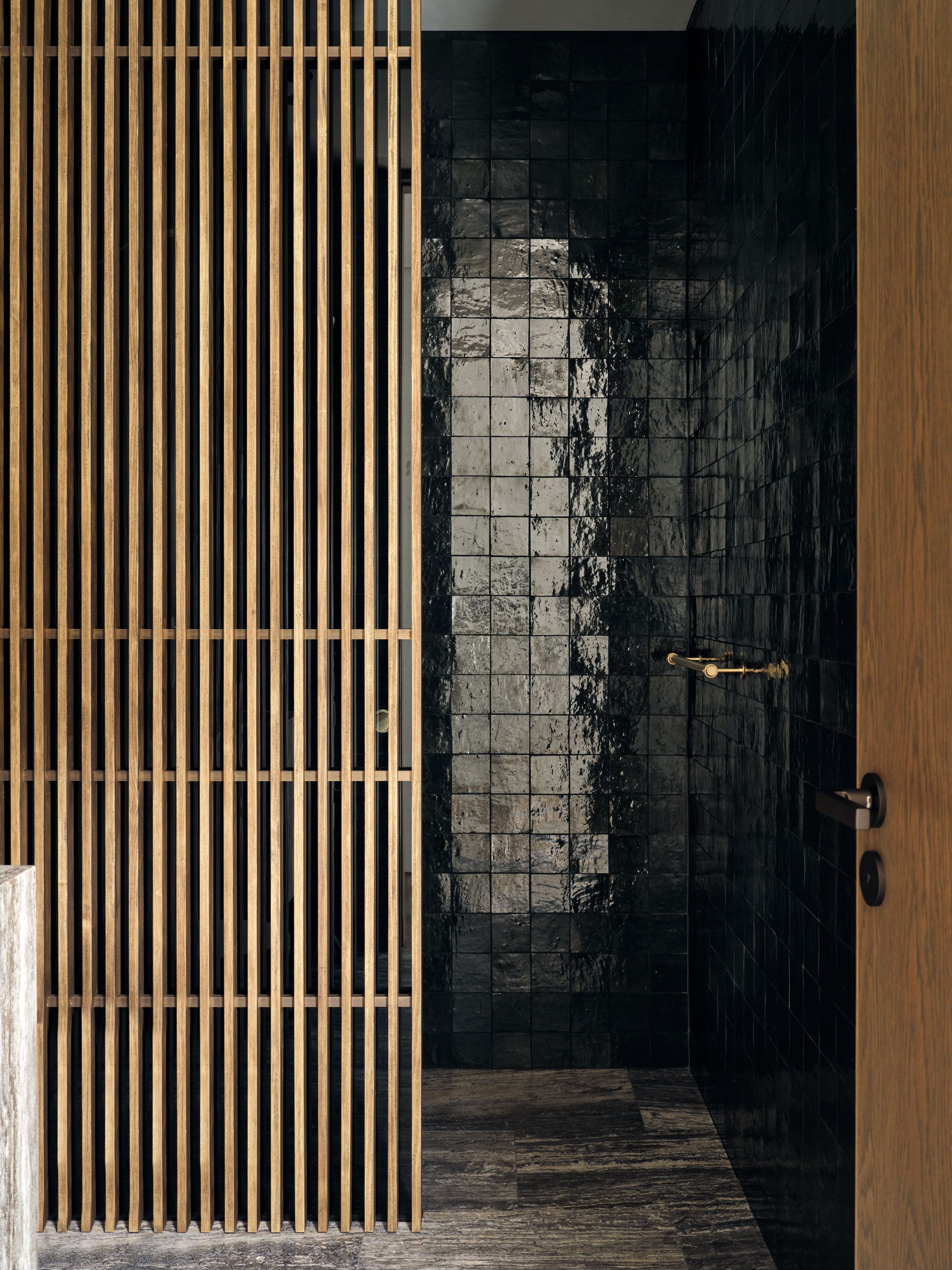 Dark tiled bathroom with deep green glossy handmade tiles, vertical timber screening and brushed brass fixtures.