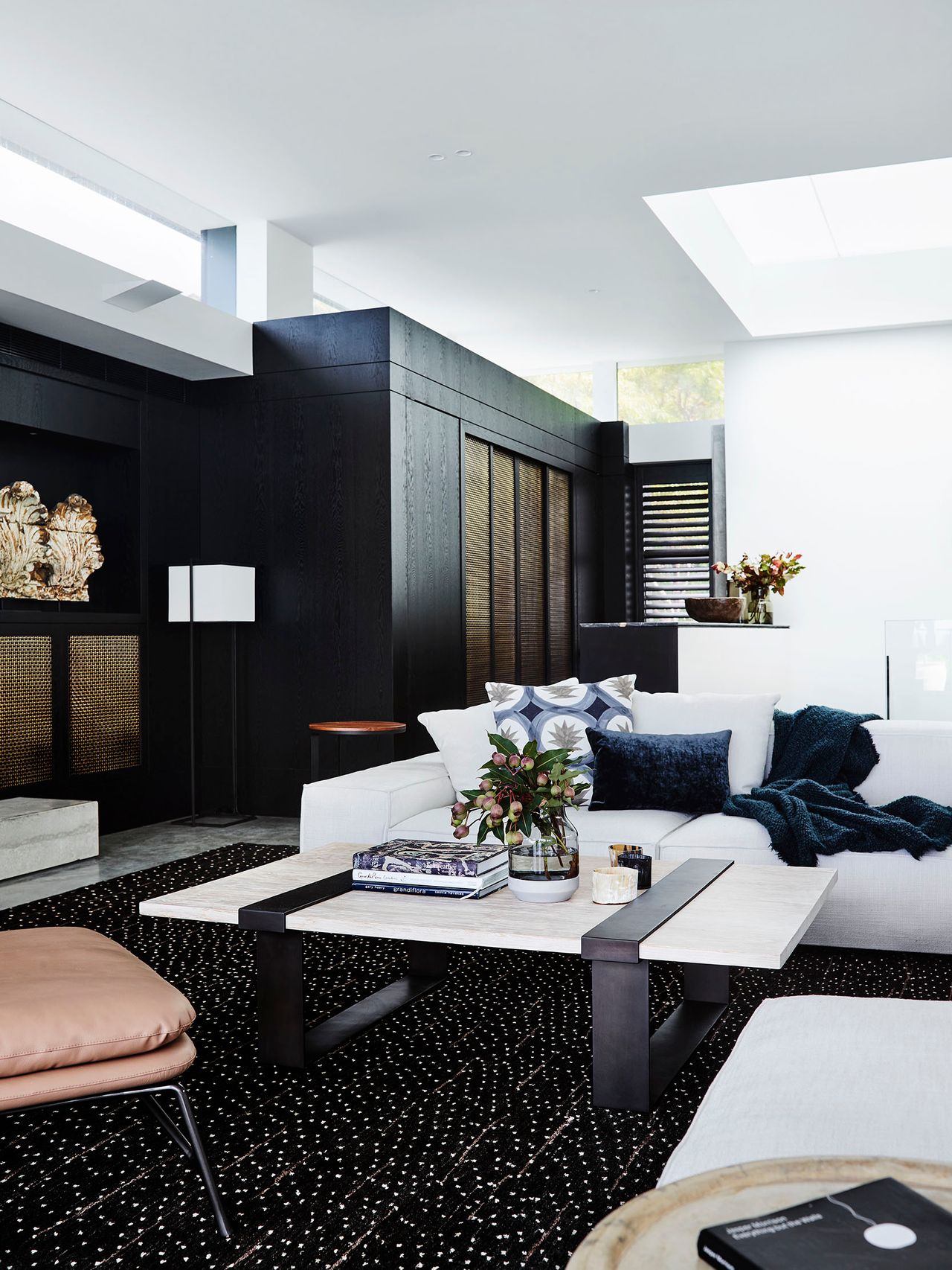 Killcare Living room with a black timber joinery wall featuring brass mesh cabinet doors and a display niche, white sectional sofa styled with navy cushions and throw, and a two-tone stone and timber coffee table on a patterned dark rug