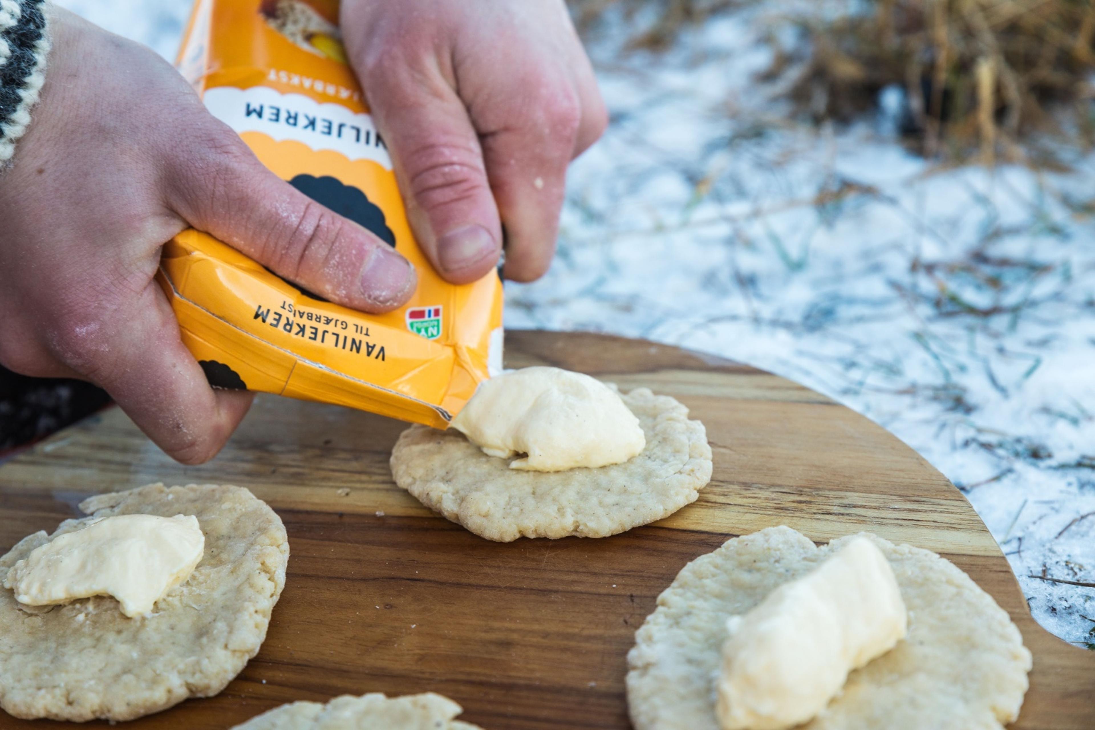 Hendene til John som presser ut vaniljekrem på bolledeig