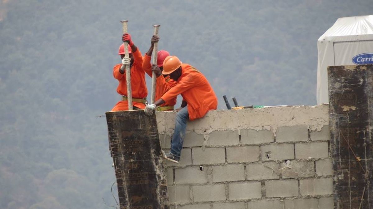 Two masons in orange overalls building a concrete block wall in Kigali