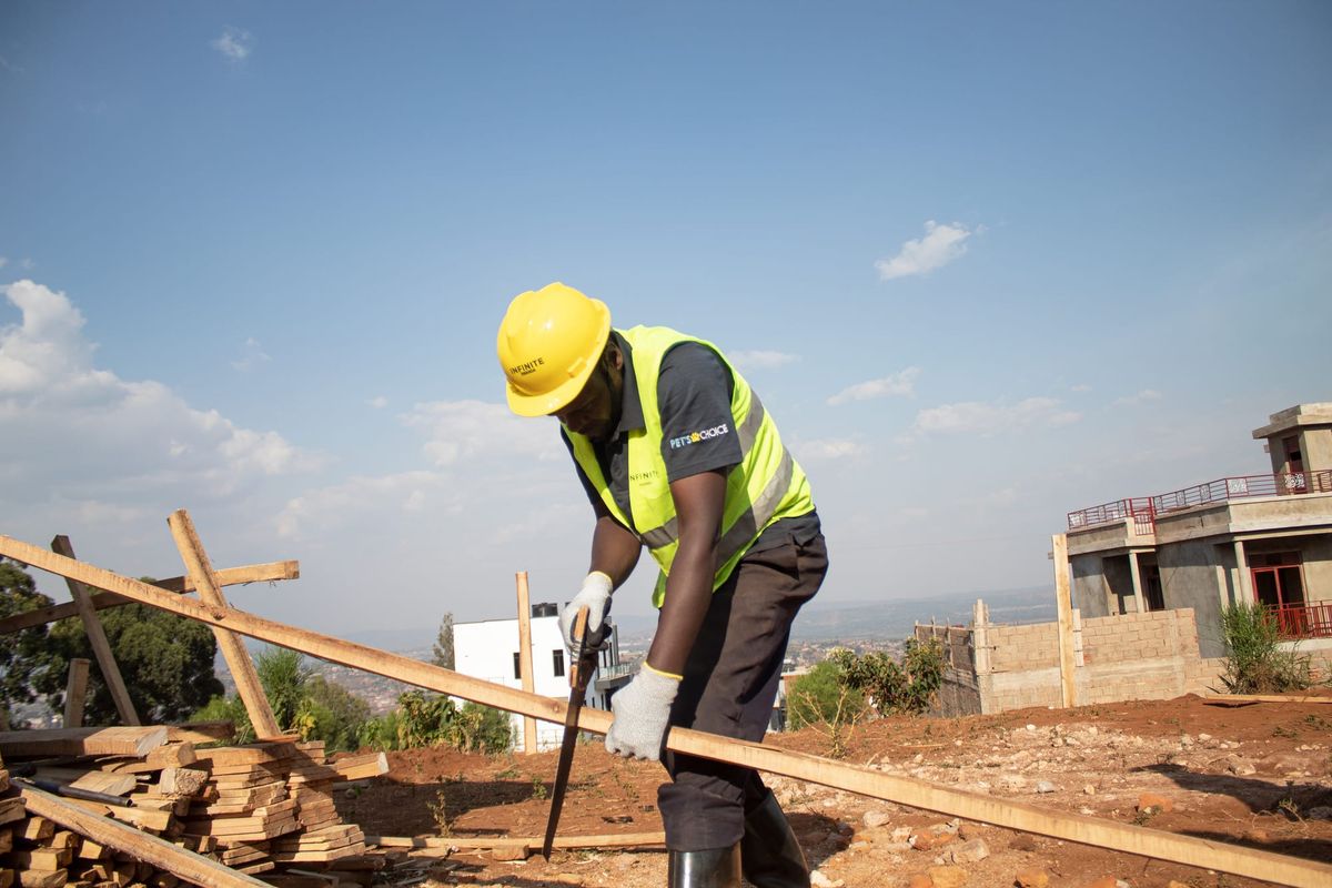 A carpenter in a hard hat and high-visibility vest sawing timber on an urban building site