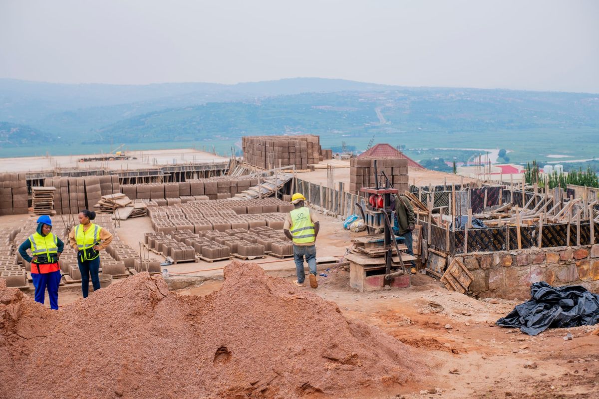 A building site in Rwanda with stacks of concrete blocks, a block-making machine and workers in high-visibility vests