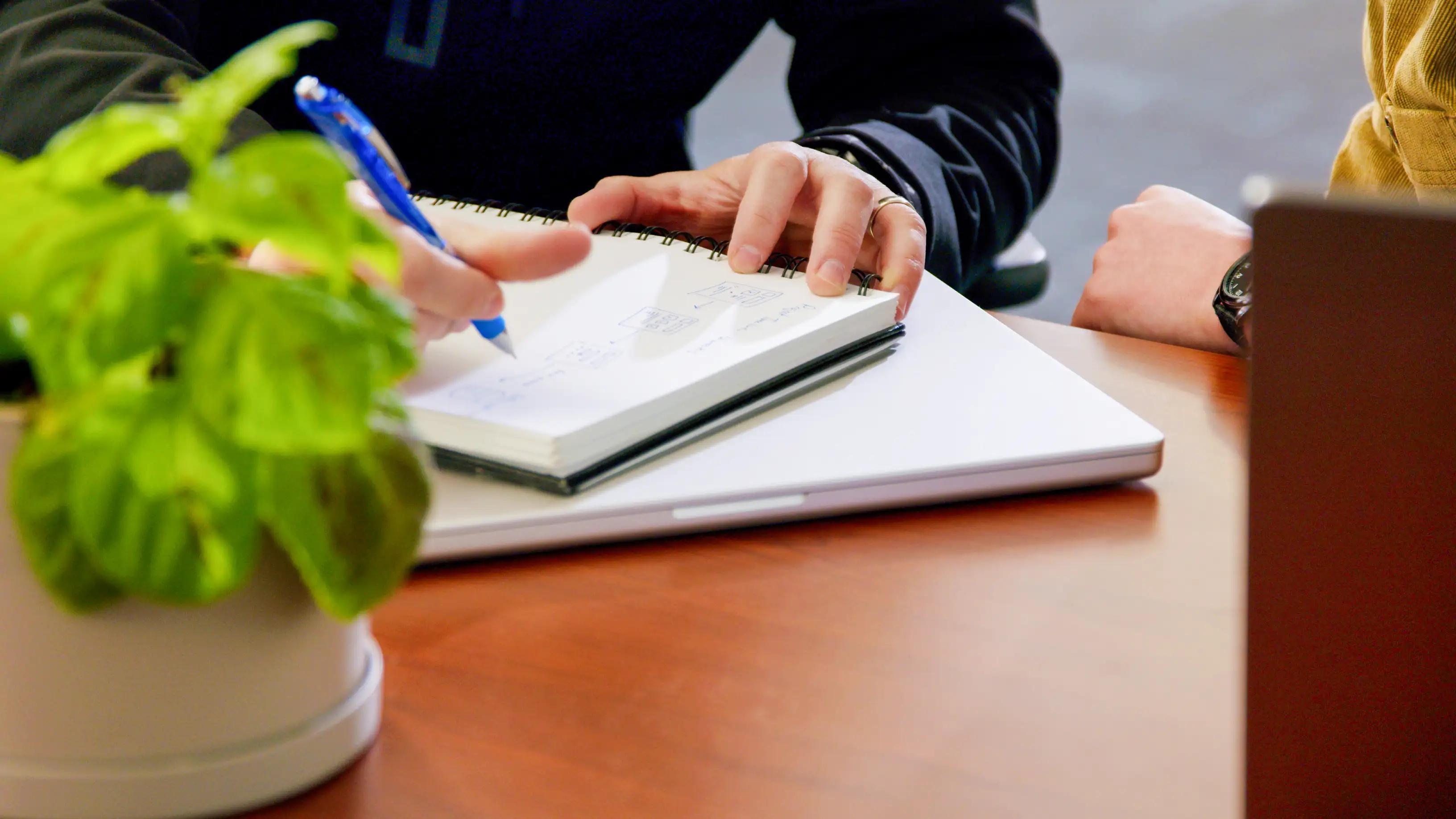 A close up of hands writing on a notebook on a desk