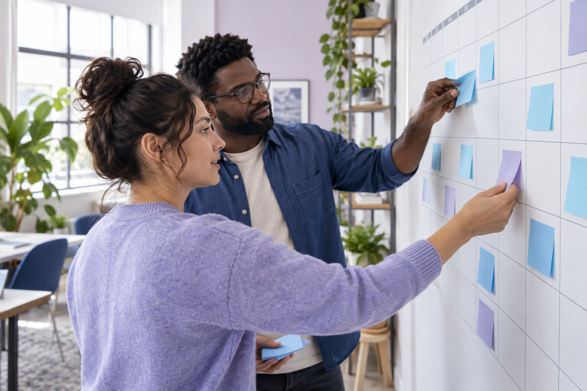 Two colleagues review blank notes on an office wall calendar while auditing recurring meetings.