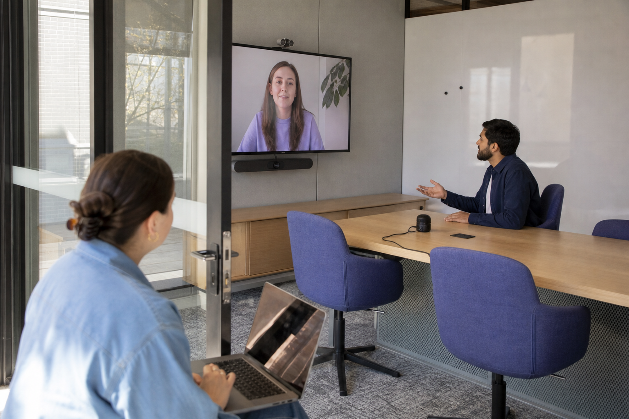 Two workplace operators test a hybrid meeting room with a remote colleague listening from the wall display.