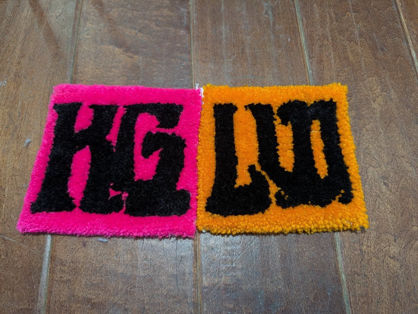 Two small square hand-tufted rugs side by side spelling KG and LW in bold black lettering on hot pink and orange backgrounds