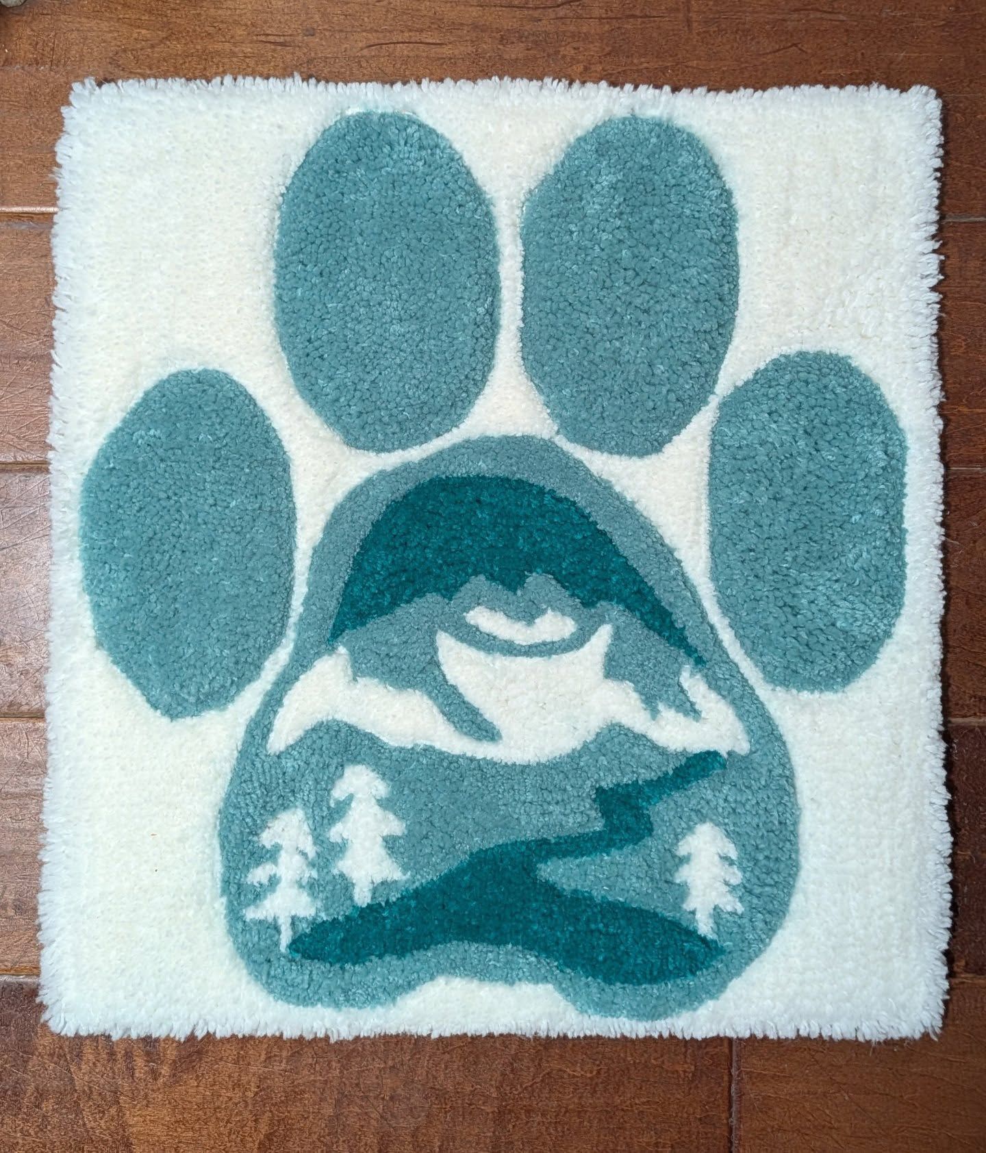 Hand-tufted rug in the shape of a paw print with a teal mountain landscape scene inside the pad, on a white background