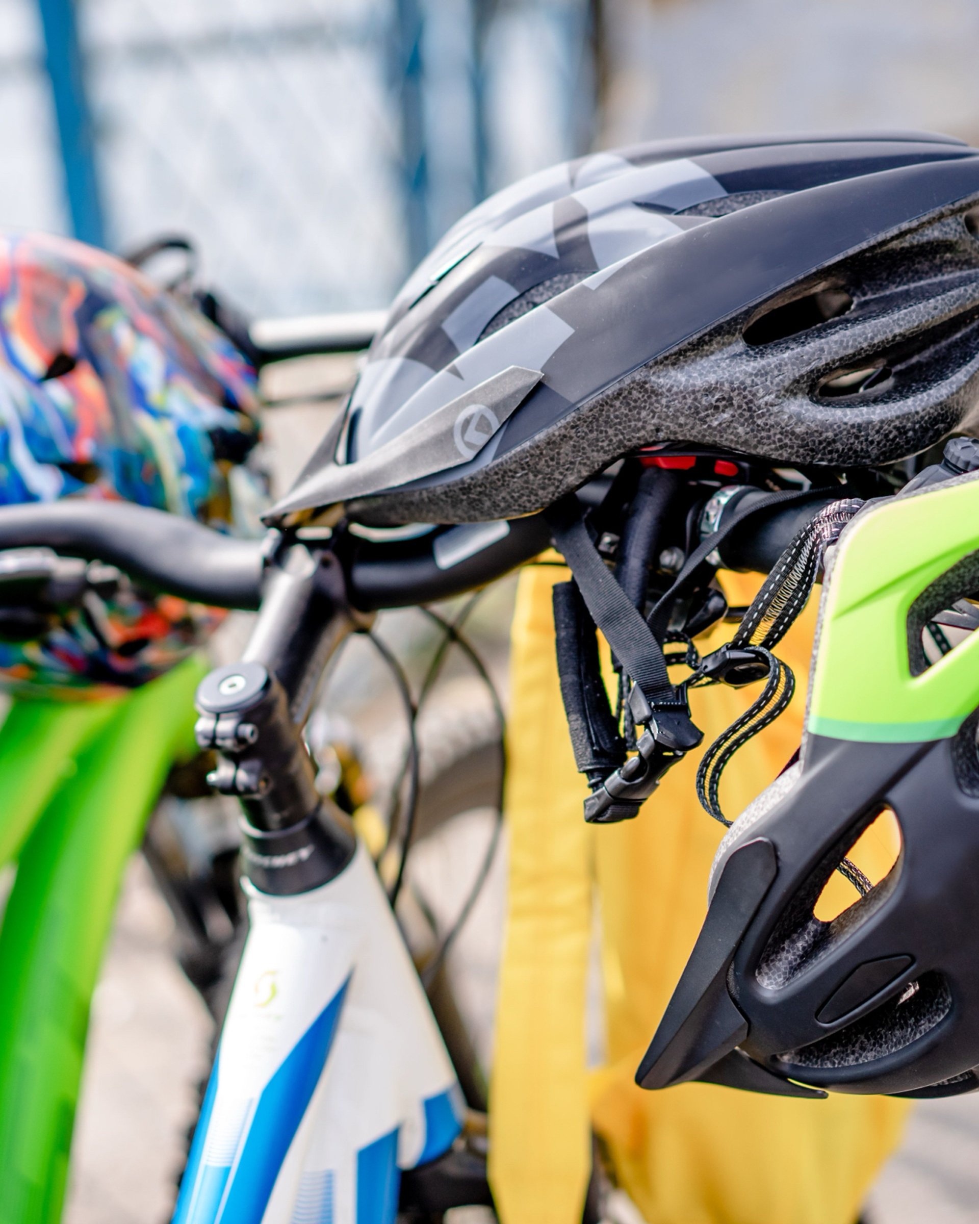 Tre cykelhjälmar som hänger på styret till uppställda cyklar.