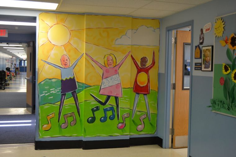 A wall mural of three children dancing with their arms raised beneath a bright sun, with musical notes at their feet.