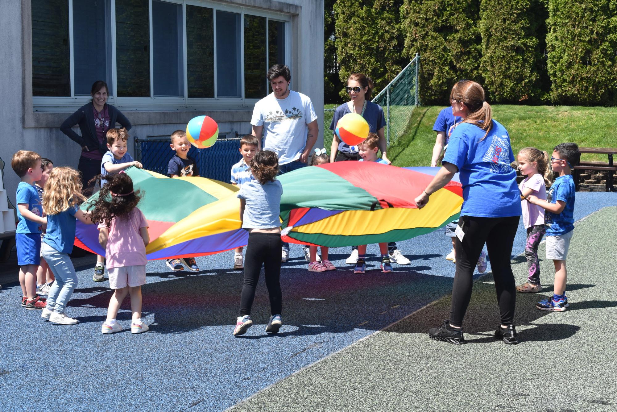 Children and staff playing with a parachute outside on the school playground