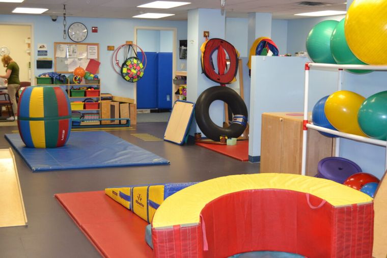 The sensory gym in the occupational and physical therapy center, with padded floor mats, a barrel roller, a suspended tire swing and racks of therapy balls.