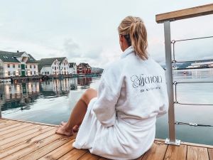 Dame som sitter på bryggen og ser mot naustene på land