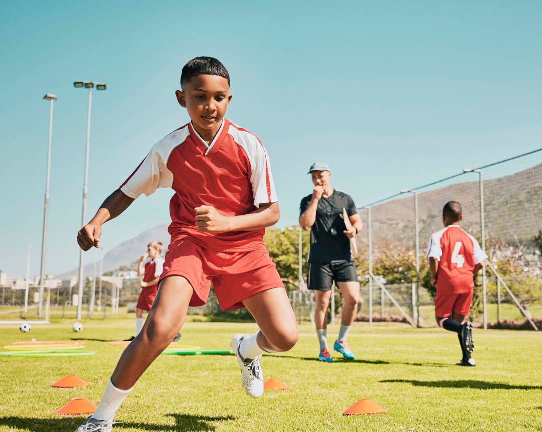 Young soccer player performing drills with coach in background