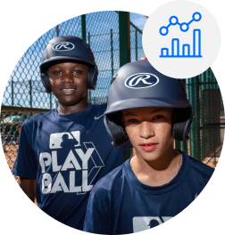 Boys smiling with baseball helmets on in a dugout