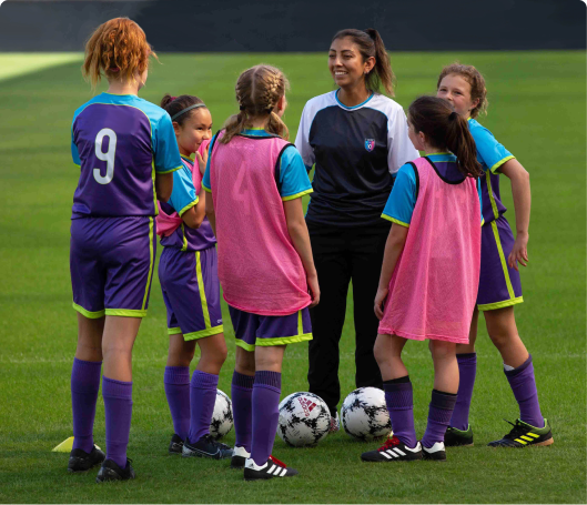Female coach speaking to circle of young, female soccer athletes