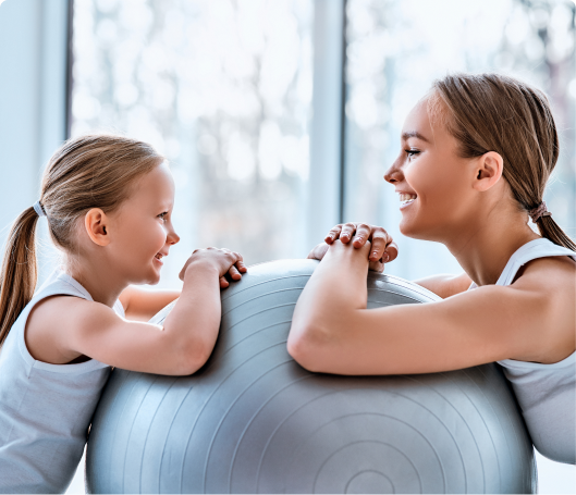 Mother and daughter facing each other using yoga ball