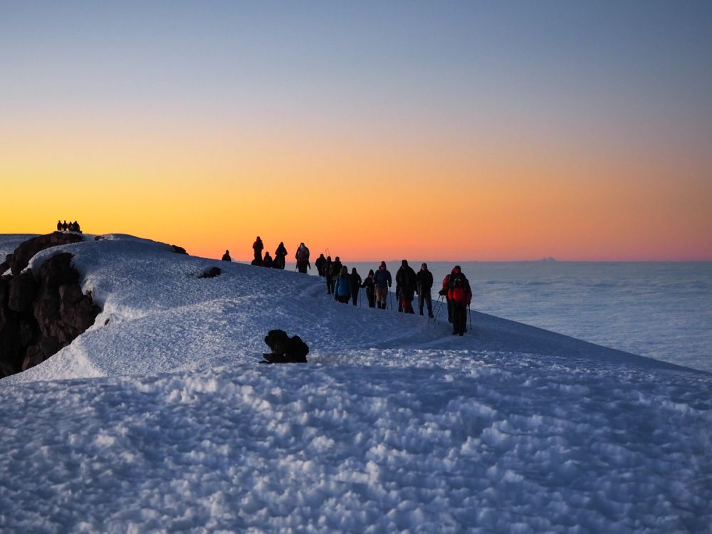 Group of trekkers silhouetted against a stunning sunrise at Kilimanjaro summit