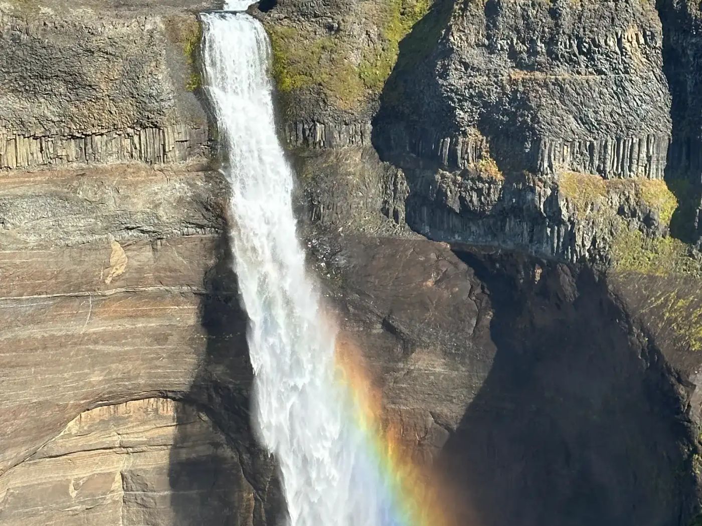 Waterfall with rainbow arcing over dramatic highland landscape