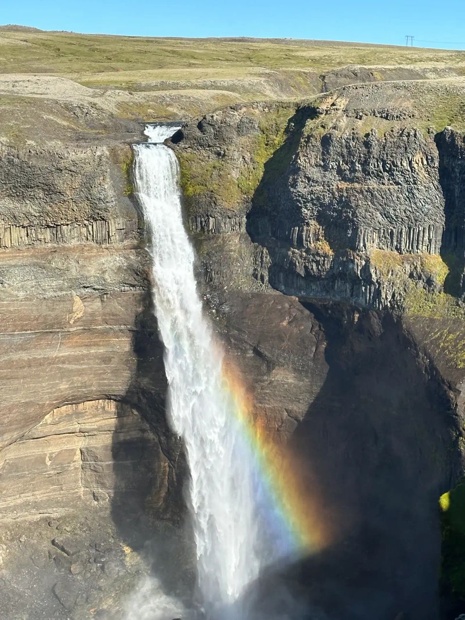 Waterfall with rainbow arcing over dramatic highland landscape