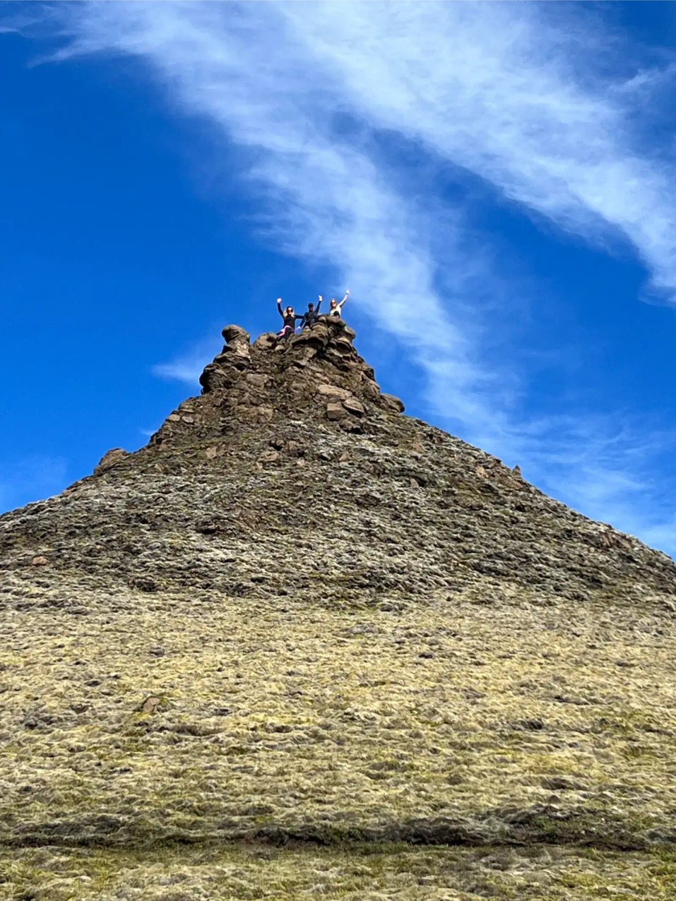 Hikers celebrating at mountain summit with arms raised in triumph
