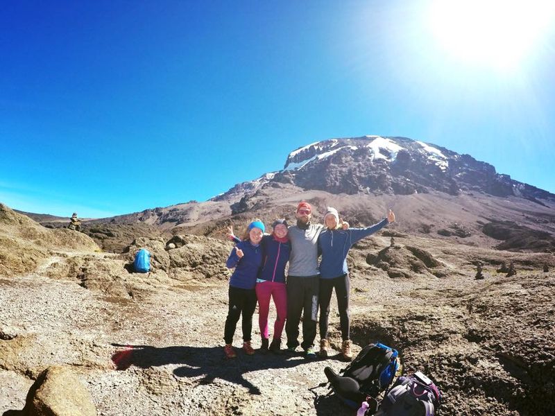 four trekkers happily pose in front of the summit