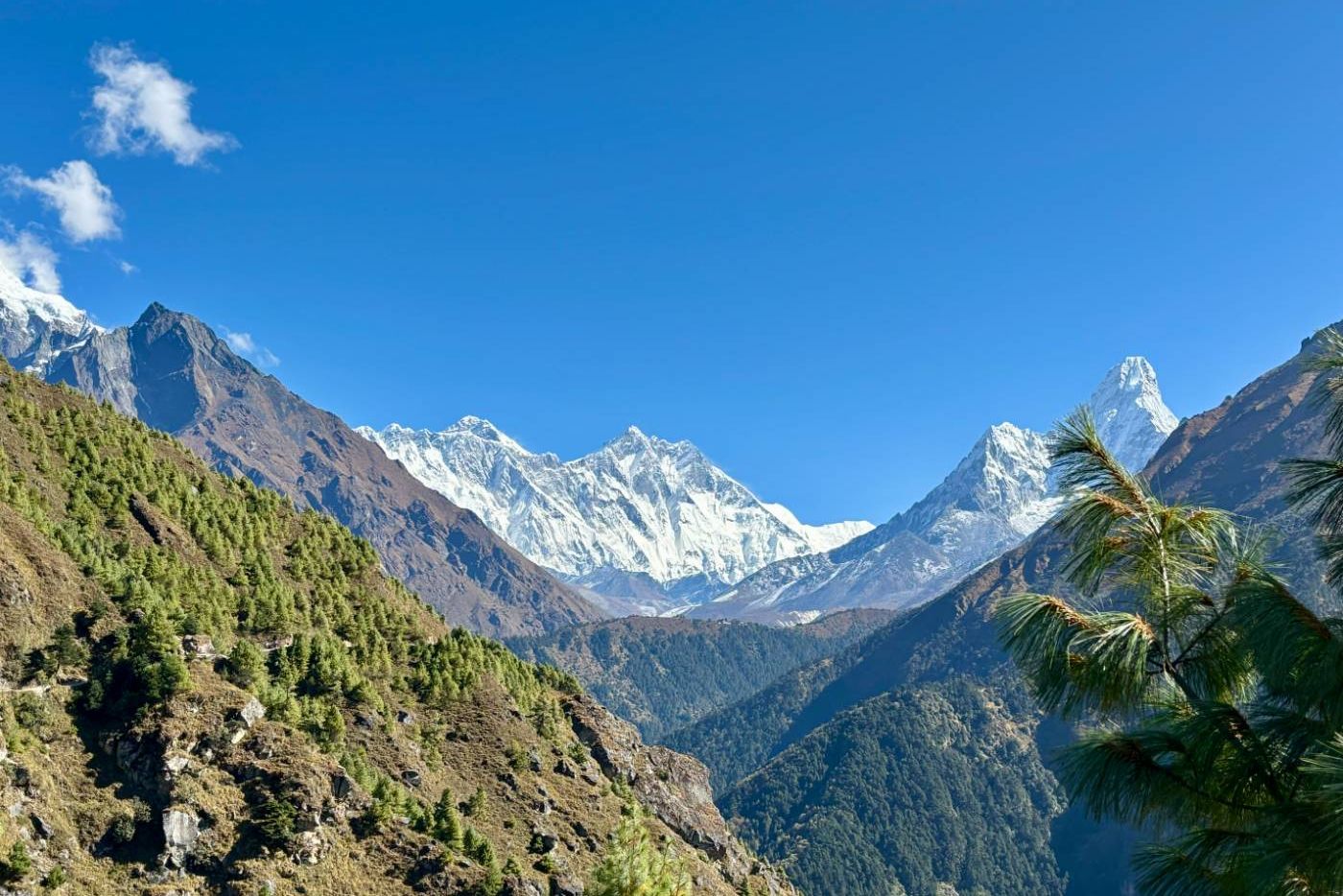 A trekker relaxing with a cup of tea in a comfortable lodge, with a stunning view of a Himalayan peak through the window.