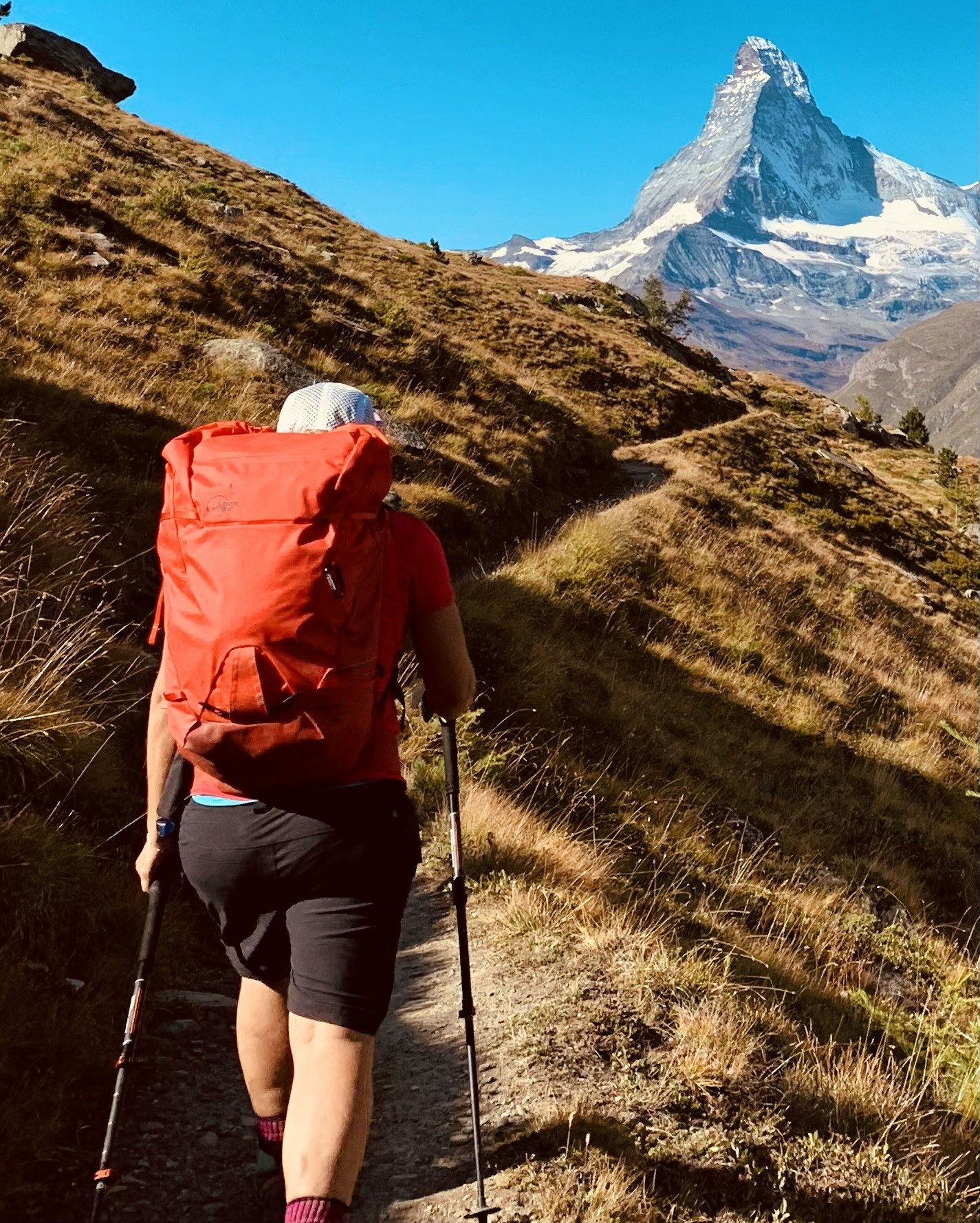 Hiker walking toward the Matterhorn on an autumn alpine trail with red backpack