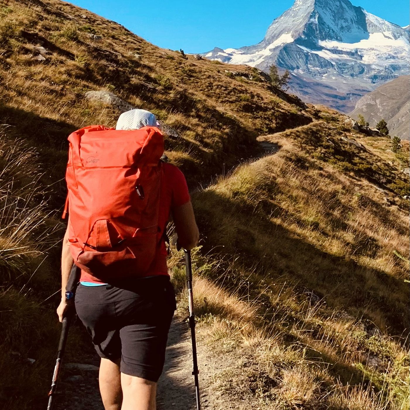 Hiker walking toward the Matterhorn on an autumn alpine trail with red backpack