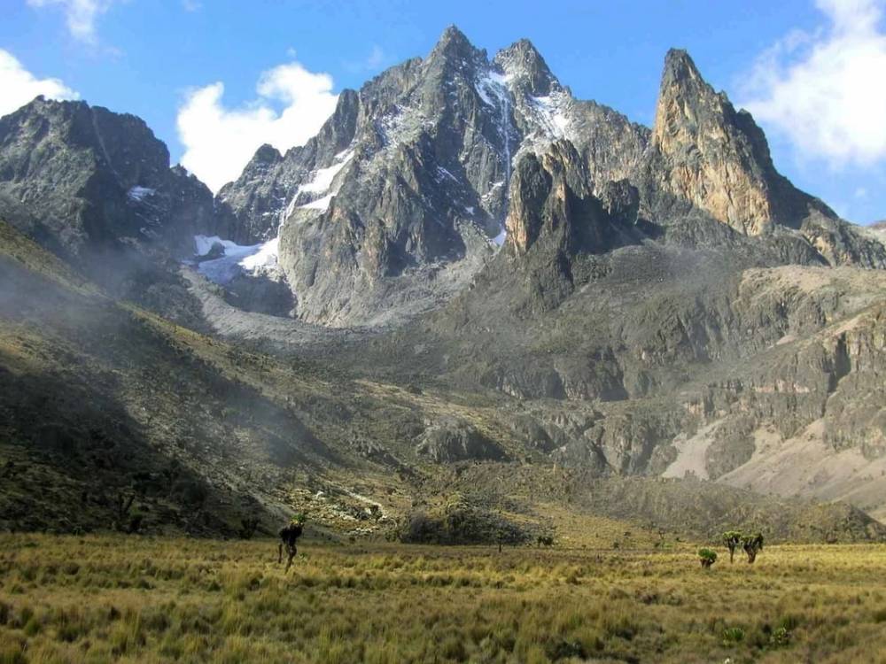 Trekkers ascending Mount Kenya's dramatic alpine landscape with rocky peaks and glaciated summit rising above the moorlands