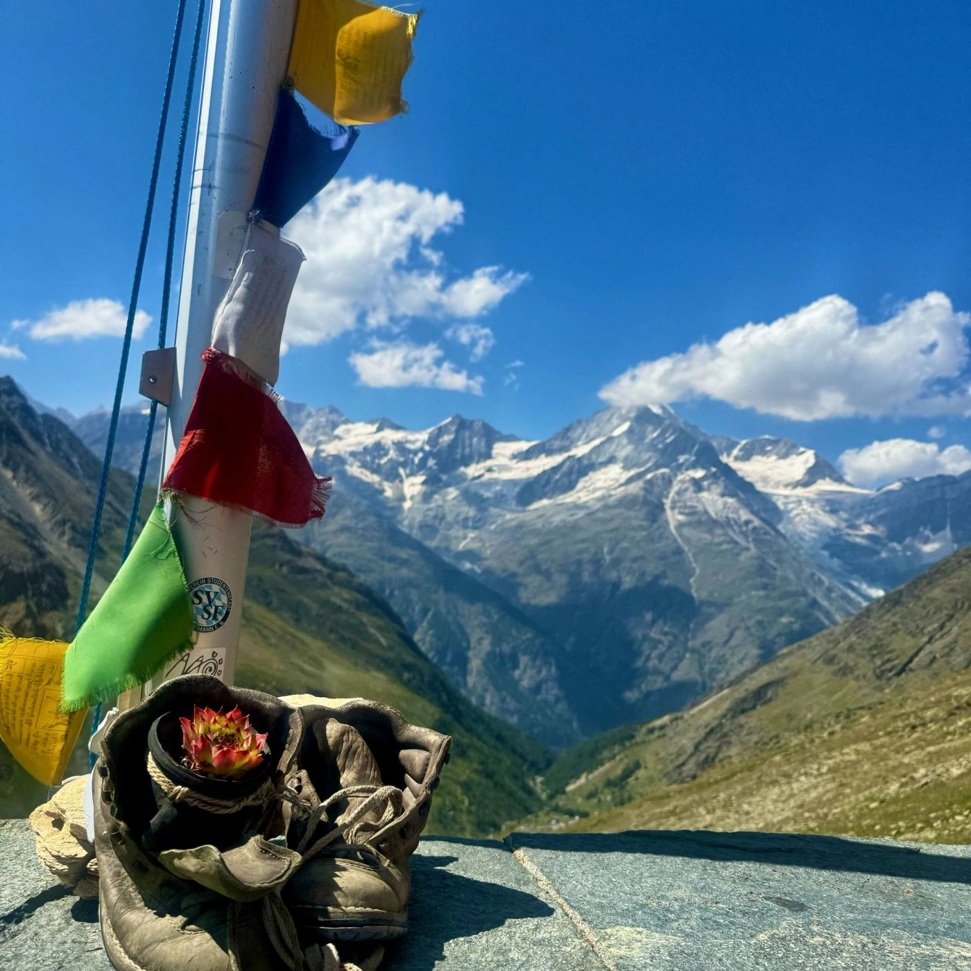 Hiking boots and prayer flags on a mountain hut terrace with panoramic valley views